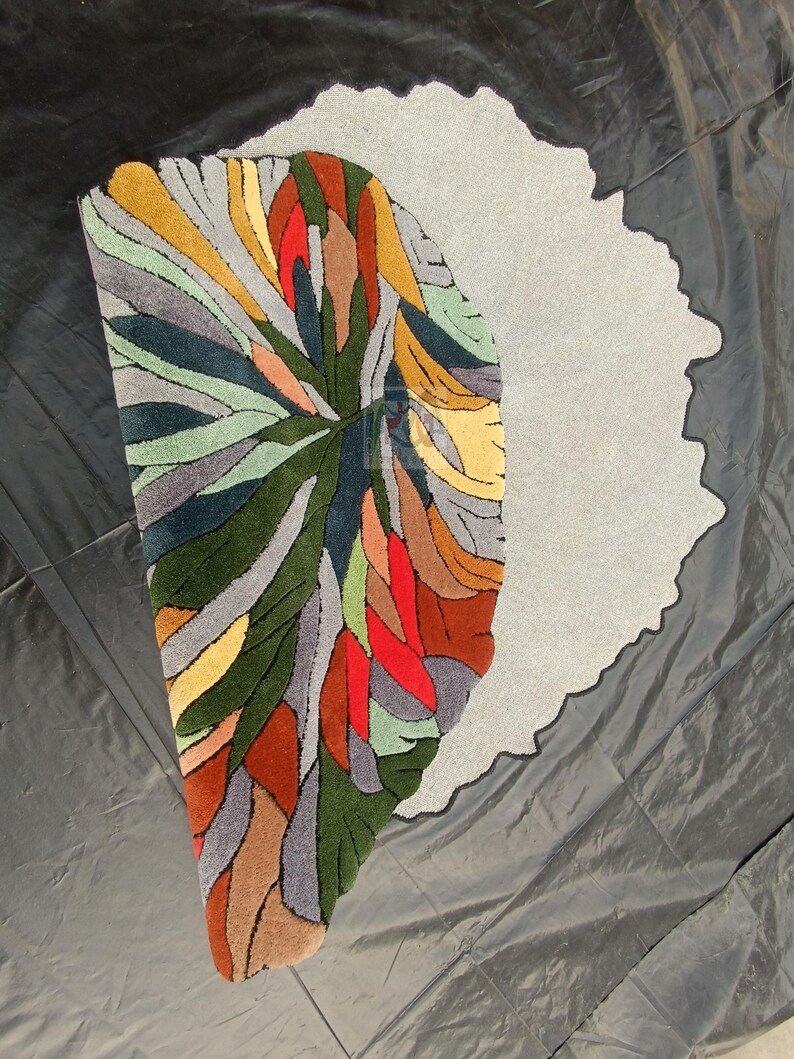 Pode incluir: Um tapete abstrato colorido com fundo cinza. O tapete &eacute; feito de l&atilde; e tem um pelo alto. O tapete tem a forma de um semic&iacute;rculo.