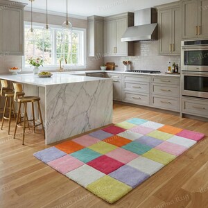 May include: A colorful, rectangular rug with a patchwork design. The rug features squares in various pastel colors, including pink, orange, yellow, and blue. The rug is placed on a hardwood floor in a kitchen setting.