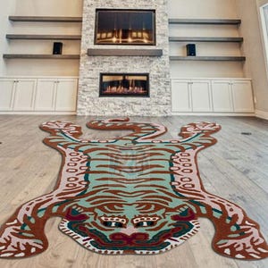 May include: A decorative rug in the shape of a tiger, featuring a brown, teal, and pink color scheme. The rug is placed on a wooden floor in a living room setting. The rug's design includes stripes and a detailed face.