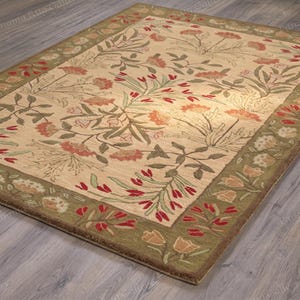 May include: A rectangular area rug featuring a cream-coloured field with a repeating floral pattern in shades of red, orange, and green. The rug has a wide olive green border decorated with a continuous motif of red and cream-coloured flowers.