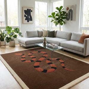 May include: A brown rectangular rug with a cream border, featuring an orange and black snake design. The rug is in a living room with a grey sofa, glass coffee table, and indoor plants. The rug's dimensions are in cm.