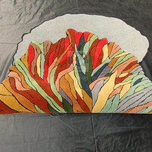 Pode incluir: Um tapete abstrato colorido com fundo cinza. O tapete &eacute; feito de l&atilde; e tem uma variedade de texturas. O tapete tem a forma de uma nuvem e um design &uacute;nico.
