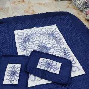 May include: A blue quilted bedspread with a white centre panel featuring a floral design. The bedspread comes with two matching pillows.