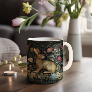 May include: A white ceramic mug with a floral pattern featuring a brown rabbit sitting in a garden. The mug has a white handle.