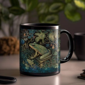 May include: Black ceramic mug featuring a detailed illustration of a green frog amidst lush foliage. The design includes various shades of green, blue, and brown, creating a nature-inspired aesthetic. The mug has a glossy finish and a black handle.