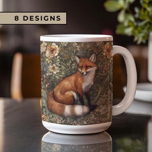 May include: A white ceramic mug with a fox illustration. The fox is sitting in a forest scene with green leaves, flowers, and vines. The mug has a handle and says "8 DESIGNS" on the front.