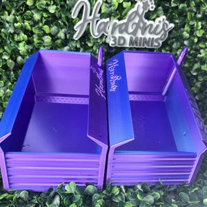 May include: Two identical purple 3D-printed storage bins with a ribbed front panel and an open top. Each bin features the text Hardini's 3D MINIS embossed on the side. The containers have a smooth interior and a distinct angular shape.