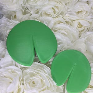 May include: Two bright green, circular, flat objects with a single wedge-shaped cutout extending from the outer edge toward the center. The surfaces are smooth with a subtle, linear texture visible across the rounded forms of these two items.