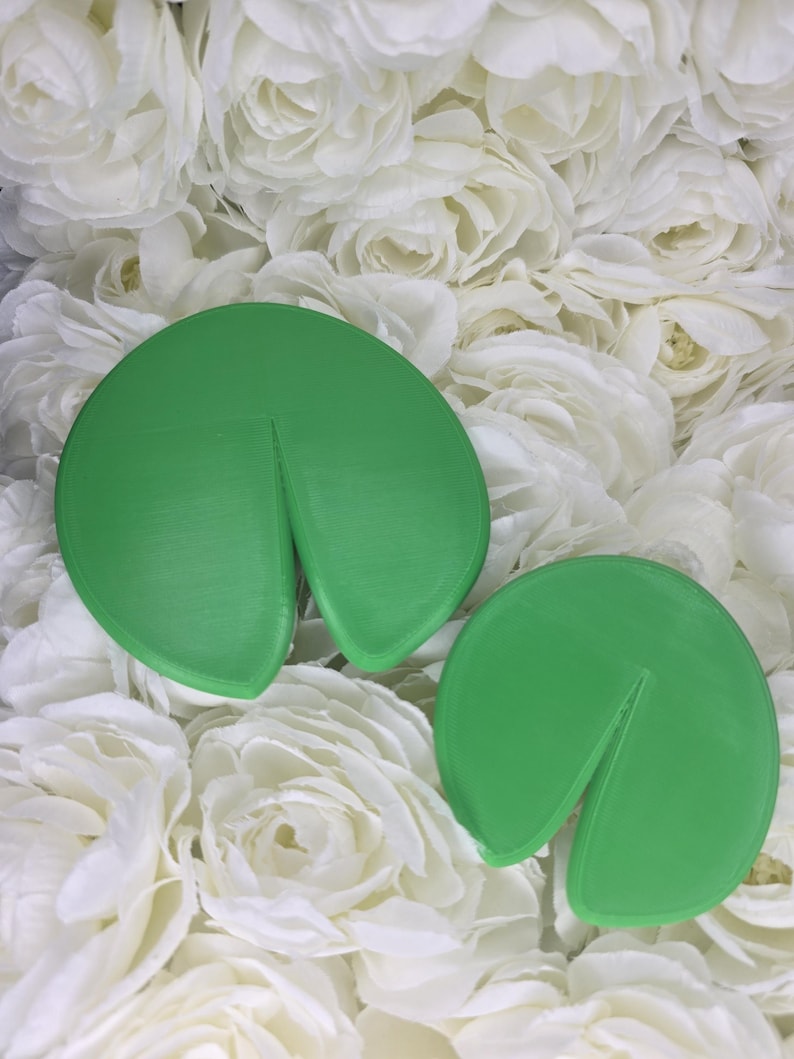 May include: Two bright green, circular, flat objects with a single wedge-shaped cutout extending from the outer edge toward the center. The surfaces are smooth with a subtle, linear texture visible across the rounded forms of these two items.