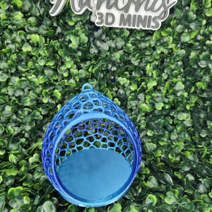 May include: A 3D printed blue egg-shaped container with a lattice-style openwork shell and a solid circular base. Above the object, a white sign with grey text reads Hardni's 3D MINIS, featuring a small star icon above the letter i.
