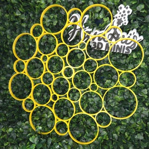 May include: A yellow, bubble-shaped 3D mini design, with the text "Hello 3D MINIS" in black and white. The design is set against a backdrop of green foliage, creating a vibrant contrast.