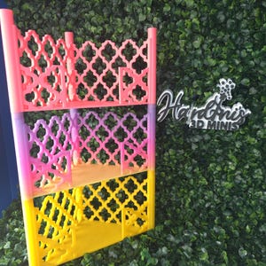 May include: A multi-tiered, colorful 3D-printed shelf with a decorative lattice design. The shelf features three levels, each in a different color: pink, purple, and yellow. The text "Hardini's 3D Minis" is visible on the right side.