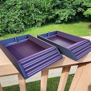 May include: Two rectangular trays with dark purple bases and dark blue frames. Each tray features a sloped front section with horizontal ridges and a small vertical post at the back edge. The interior surfaces are smooth and flat with a deep purple finish.
