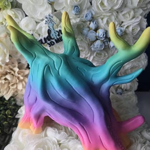 May include: A multi-colored, gradient-style 3D printed creature figurine featuring a smooth, organic, tree-like texture. The colors transition from yellow at the base to green, teal, blue, and purple, with prominent horn-like protrusions extending upward.