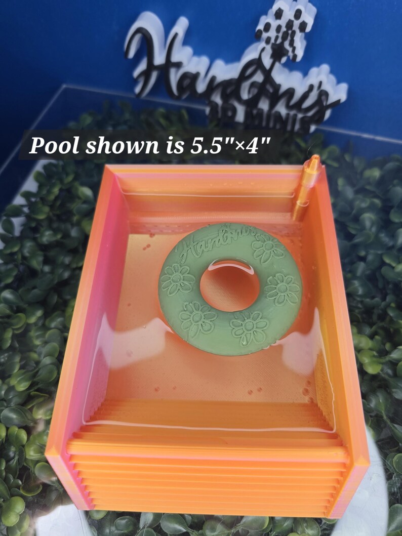 May include: A rectangular orange and pink pool measuring 5.5 inches by 4 inches, containing a green circular float with a floral pattern and the text Hardin's. The pool features a small orange post in one corner and a clear liquid interior.