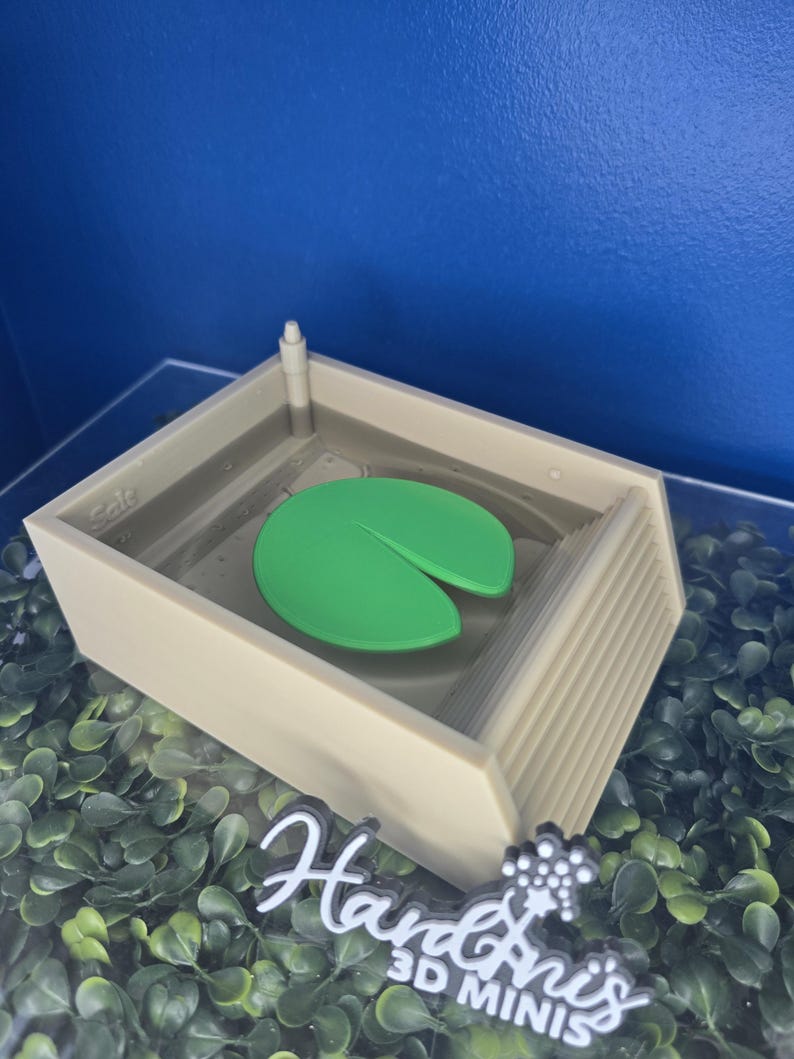 May include: A beige rectangular pool structure with a single green lily pad floating in the center. The pool features a small pillar in one corner, a set of steps on one side, and the word "Sale" embossed on the inner wall. A white logo reads "Hardinis 3D MINIS".