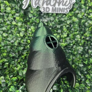 May include: A 3D-printed plague doctor mask in shades of green and black. The mask features a long beak, a circular eye opening with a cross design, and the text "Hard Knis 3D MINIS" in white.