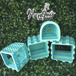 May include: A collection of 3D-printed mini structures in shades of blue and green. The designs include a small square with a lattice top, and several open-sided boxes with striped detailing. The background is a dense green foliage.