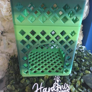 May include: A square, open-top storage crate featuring a lattice pattern on all sides and a base. The crate displays a gradient color transition from a light lime green at the bottom to a darker forest green at the top rim. A small black sign reads Hardinis 3D Minis.