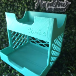 May include: A turquoise 3D-printed organizer with a two-tiered design. The top tier has curved cutouts, and the sides feature a lattice pattern. The name "Hardins 3D Minis" is visible in the background.