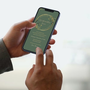 May include: A smartphone displays a green invitation with gold floral accents and text in German. The phone is held by a person, with a finger touching the screen. The invitation is for a Christmas party.