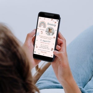Op de afbeelding: Een smartphone die een kleurrijke verjaardagsuitnodiging toont met een regenboog, vlaggetjes en een foto van een jong kind. De uitnodigingstekst luidt "Einladung" en bevat de datum "12. August 2024".