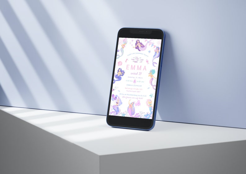 May include: A smartphone displays a mermaid-themed invitation with the text "EMMA wird 3!". The invitation features illustrations of mermaids, stars, and aquatic elements in shades of purple, pink, and blue. The phone has a blue frame.