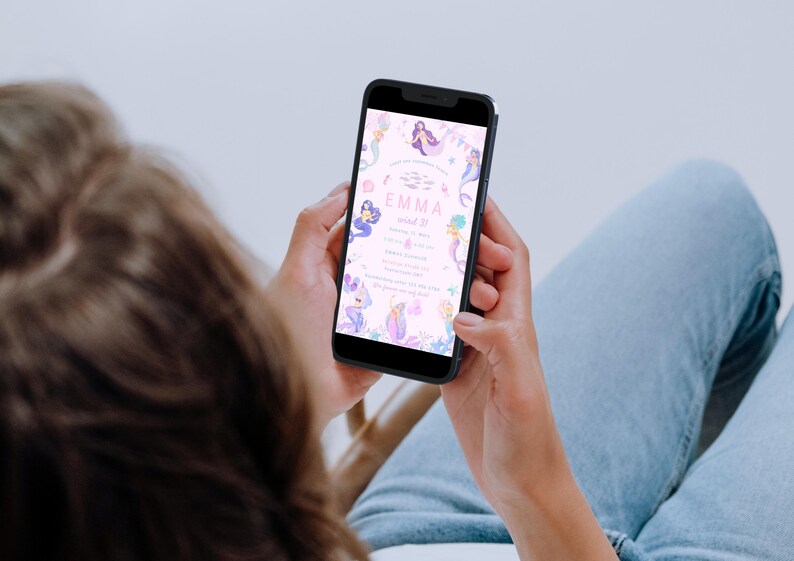 May include: A smartphone displays a mermaid-themed birthday invitation. The invitation features illustrations of mermaids, fish, and aquatic plants in shades of purple, blue, and pink. The text reads "Emma, wird 3!" and includes event details.