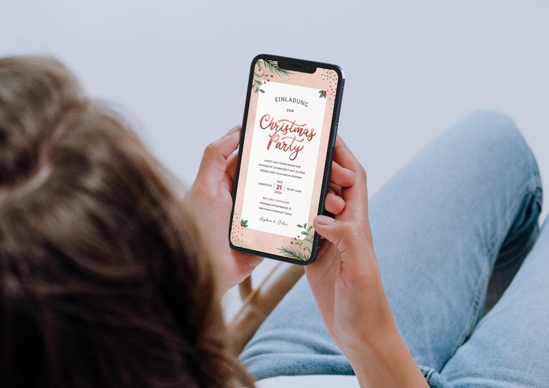 May include: A person is looking at a smartphone screen displaying a Christmas party invitation with a pink background and green and red floral accents. The invitation text reads "Einladung zur Christmas Party".