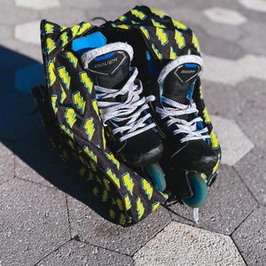 May include: Black and yellow hockey bag with a lightning bolt pattern. Two black and white hockey skates are inside the bag. The text "CARRY EXTRA VIBES" is at the bottom of the image.