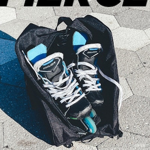 May include: A black hockey bag with two pairs of black and blue ice skates with white laces inside. The bag has a zipper and a handle.