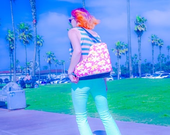 May include: A person with pink and orange hair wearing a striped tank top and blue jeans is roller skating on a sidewalk. They are wearing a pink and yellow floral backpack and yellow roller skates with pink wheels.