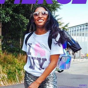 May include: A woman wearing a white t-shirt with a pink roller skate graphic and the text "I NY" is walking down a street. She is carrying a clear iridescent backpack with black straps. The backpack has a mesh water bottle holder and a zippered pocket. The text "FEATURES:" is visible in the lower right corner of the image. The text below "FEATURES:" describes the backpack's features, including heavy-duty construction, a 1.0 liter water bottle mesh bag, interior stash pockets, heavy-duty reinforced tarpaulin lining, and an interior skate restraint strap.