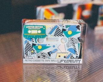 May include: A retro cassette tape wallet with a colorful geometric design in a clear plastic case. The wallet features a zipper closure and the text "LIMITED EDITION COLLECTION" and "RETRO CASSETTE TAPE WALLET FYDELITY".