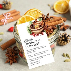 Könnte beinhalten: Ein Glasgefäß gefüllt mit einem weihnachtlichen, köchelnden Potpourri, einschließlich Zimtstangen, Sternanis, Orangenscheiben und anderen Gewürzen. Das Gefäß trägt ein Etikett mit der Aufschrift "Holiday Simmering Potpourri" und enthält Anweisungen zur Verwendung. Das Etikett enthält auch den Text "From the home of ANNA GREY".
