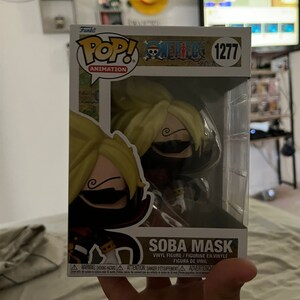 May include: A Funko Pop! Animation vinyl figure of Soba Mask from One Piece. The figure is in a clear plastic display case. The figure has blonde hair, a black mask, and a red and black outfit. The box has the number 1277.