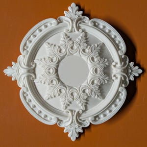 May include: A white circular ceiling medallion featuring intricate relief carvings of acanthus leaves and a beaded border. The design includes a smooth central disc surrounded by symmetrical floral patterns that extend toward the outer edge.