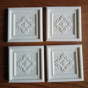 Peut inclure: Quatre dalles de plafond blanches avec un motif orné en forme de diamant surélevé au centre de chaque dalle.