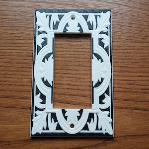 Puede incluir: Una tapa de interruptor de luz decorativa en blanco y negro con un diseño floral.