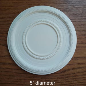 Peut inclure: Médaillon de plafond blanc avec un design décoratif en relief. Le médaillon a un diamètre de 12,7 cm.
