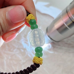 Peut inclure: Un bracelet en jade avec un charme de tortue, des perles vertes et jaunes sur un cordon marron.