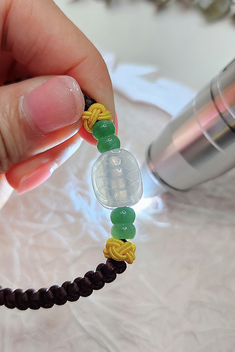 Peut inclure: Un bracelet en jade avec un charme de tortue, des perles vertes et jaunes sur un cordon marron.