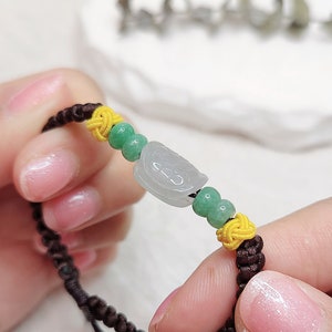 Peut inclure: Un bracelet en cordon marron avec des perles vertes et jaunes. Le bracelet est orn&eacute; d'un pendentif en jade avec un motif sculpt&eacute;.