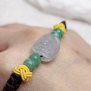 Peut inclure: Un bracelet en jade avec une perle de jade vert clair et un pendentif en jade blanc. Le bracelet est fait avec une ficelle brune et jaune.