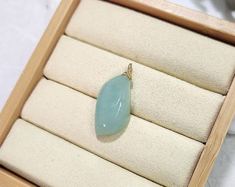 May include: A light blue gemstone pendant with a gold bail, displayed in a wooden ring box with beige velvet lining.
