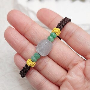 Peut inclure: Un bracelet en cordon marron avec des perles vertes et jaunes et un pendentif en jade blanc avec un motif sculpt&eacute;.