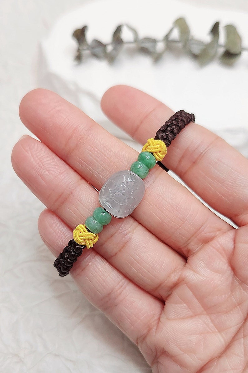 Peut inclure: Un bracelet en cordon marron avec des perles vertes et jaunes et un pendentif en jade blanc avec un motif sculpt&eacute;.