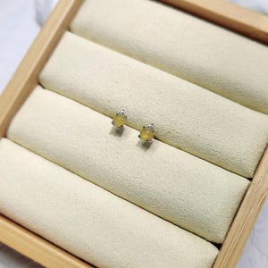 Puede incluir: Un par de pequeños pendientes redondos de piedra amarilla con engaste de plata. Los pendientes se muestran en una caja de madera con un forro de terciopelo blanco.