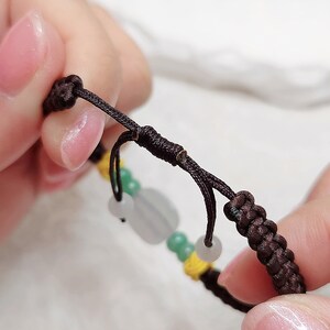 Peut inclure: Un bracelet en cordon marron avec des perles vertes et blanches. Le bracelet a un n&oelig;ud &agrave; l'extr&eacute;mit&eacute;.