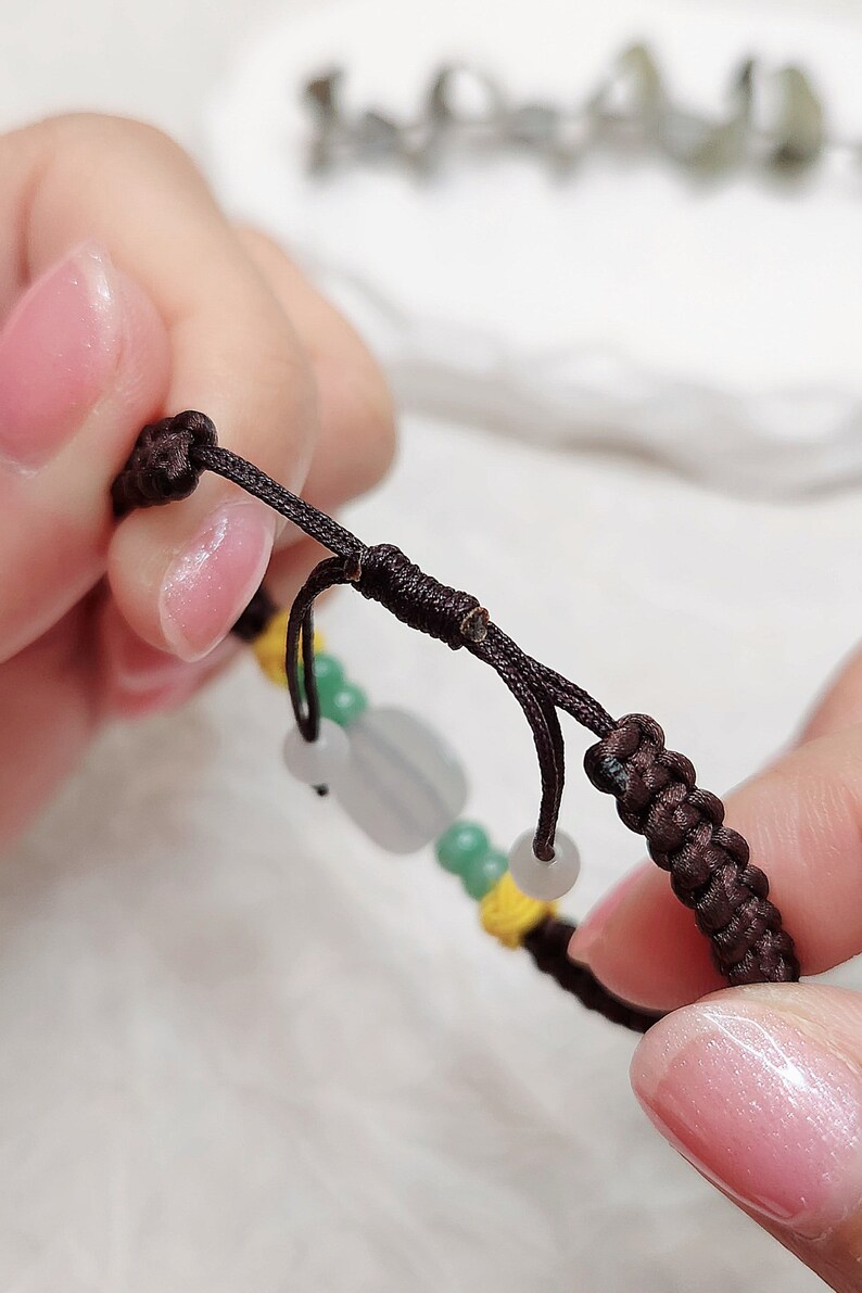 Peut inclure: Un bracelet en cordon marron avec des perles vertes et blanches. Le bracelet a un n&oelig;ud &agrave; l'extr&eacute;mit&eacute;.